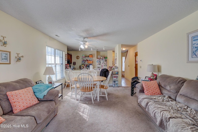 living room with light carpet, ceiling fan, visible vents, and a textured ceiling