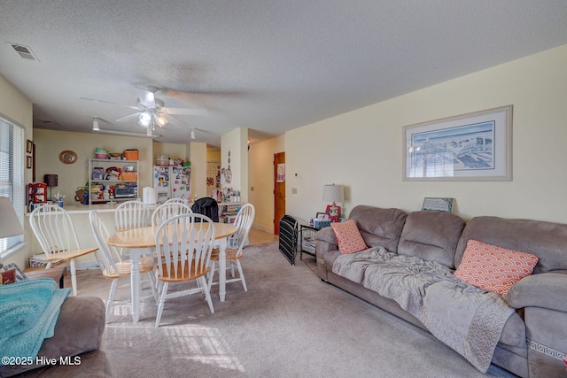 carpeted living area with a healthy amount of sunlight, a ceiling fan, visible vents, and a textured ceiling