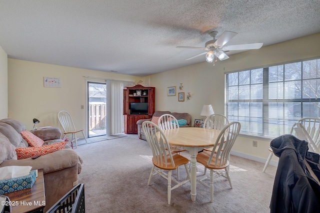 dining area featuring a textured ceiling, baseboards, a ceiling fan, and light colored carpet