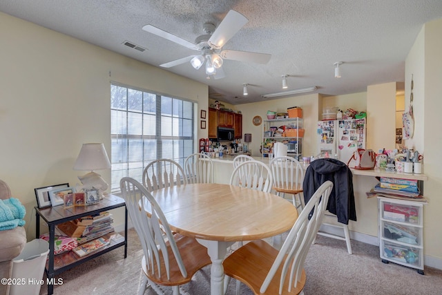 dining space featuring a textured ceiling, ceiling fan, light carpet, visible vents, and baseboards