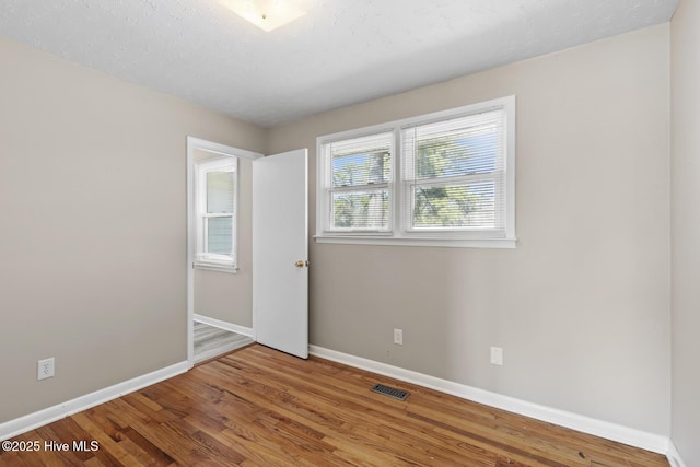 empty room with baseboards, a textured ceiling, visible vents, and wood finished floors