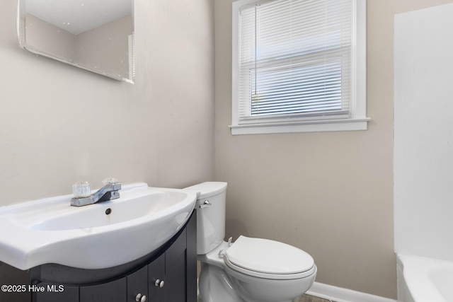 bathroom featuring a washtub, vanity, toilet, and baseboards