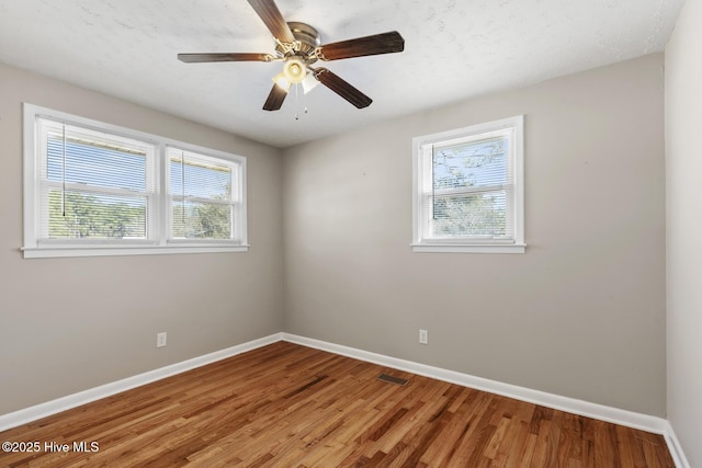 empty room featuring a ceiling fan, visible vents, baseboards, and wood finished floors