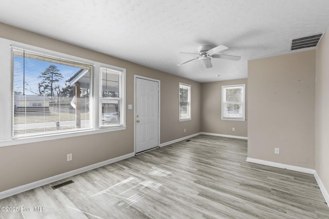 interior space featuring a ceiling fan, light wood-style flooring, visible vents, and baseboards