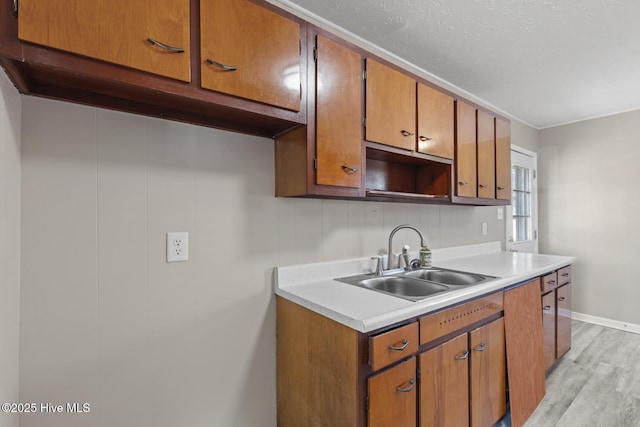 kitchen with baseboards, brown cabinetry, light countertops, light wood-type flooring, and a sink