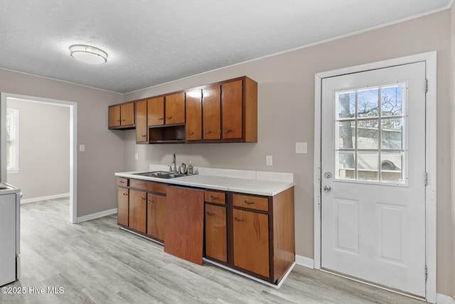 kitchen with brown cabinetry, light wood-style floors, light countertops, and a sink