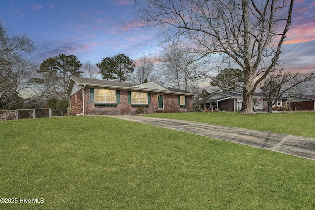 ranch-style home with a yard, concrete driveway, brick siding, and fence