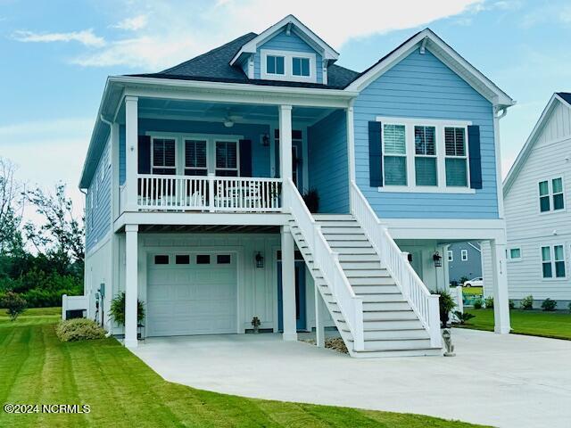 beach home with driveway, covered porch, stairs, and a front lawn