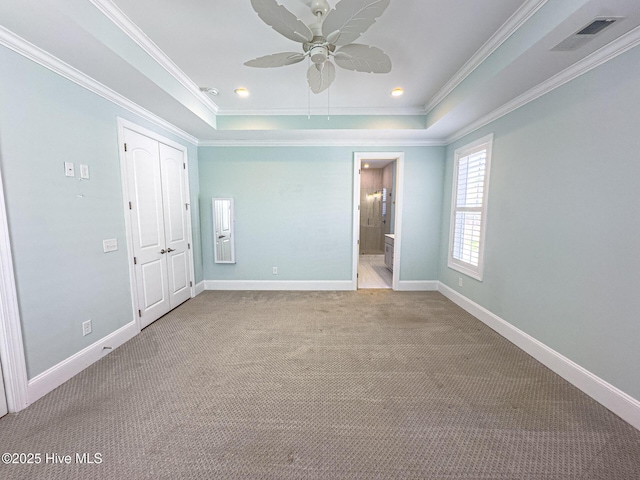 unfurnished bedroom featuring carpet, visible vents, a raised ceiling, and ornamental molding