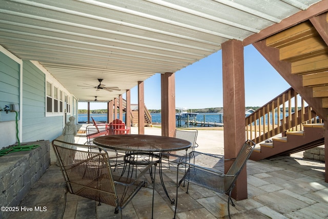 view of patio featuring outdoor dining space, stairway, a water view, and a ceiling fan