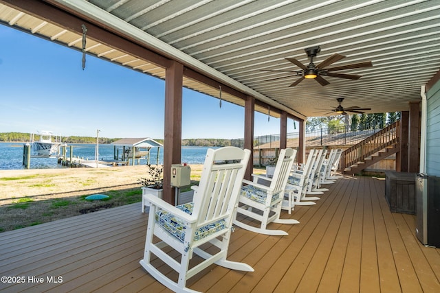 wooden terrace featuring boat lift, a water view, stairway, ceiling fan, and a boat dock