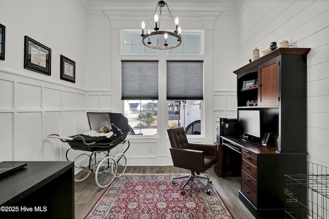 office with a towering ceiling, an inviting chandelier, a decorative wall, and wood finished floors