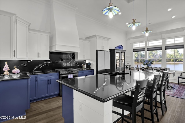 kitchen featuring dark countertops, refrigerator, blue cabinetry, premium range hood, and a sink