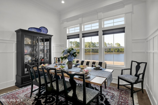 dining area featuring a wainscoted wall, ornamental molding, dark wood-type flooring, a water view, and a decorative wall