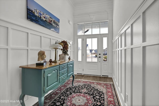 foyer entrance featuring crown molding, a high ceiling, wood finished floors, and a decorative wall