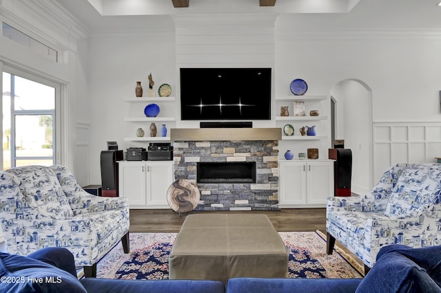 living room with a stone fireplace, built in features, crown molding, and wood finished floors