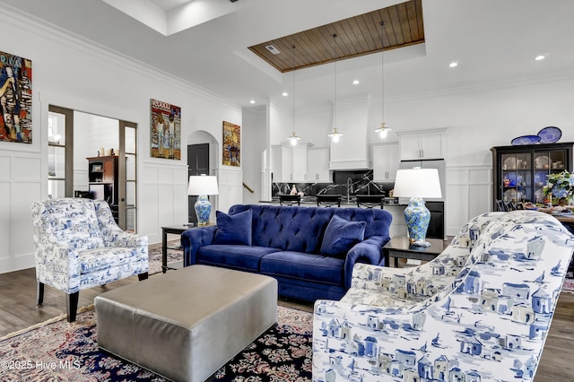 living room featuring a tray ceiling, dark wood-style flooring, a decorative wall, and arched walkways