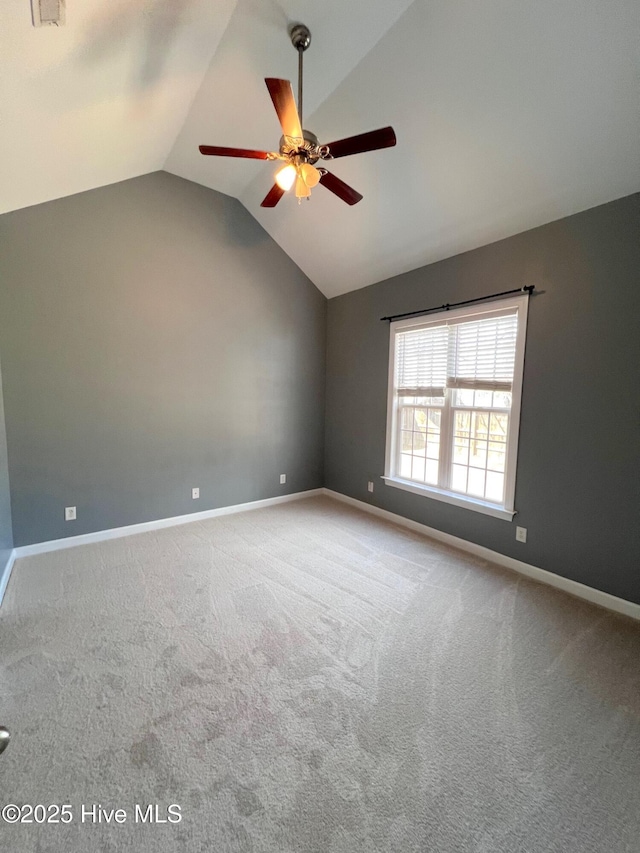 carpeted spare room featuring lofted ceiling, baseboards, and a ceiling fan