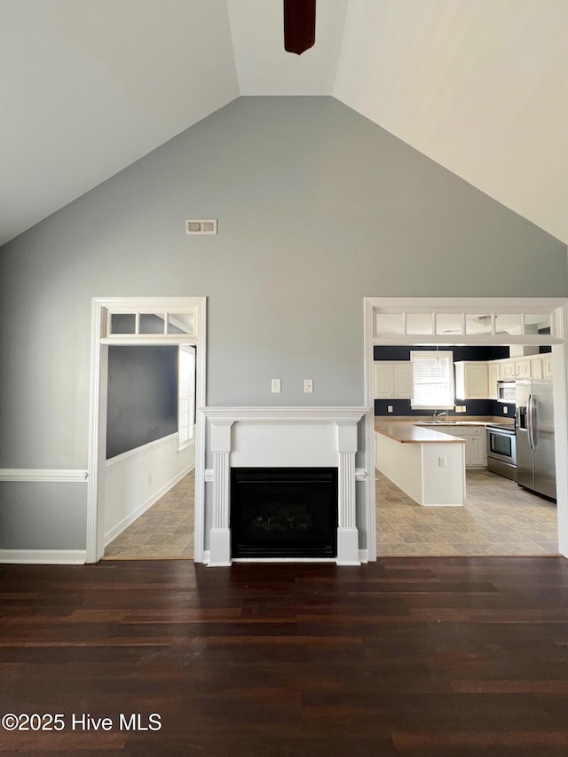 unfurnished living room with high vaulted ceiling, a fireplace, a sink, wood finished floors, and visible vents