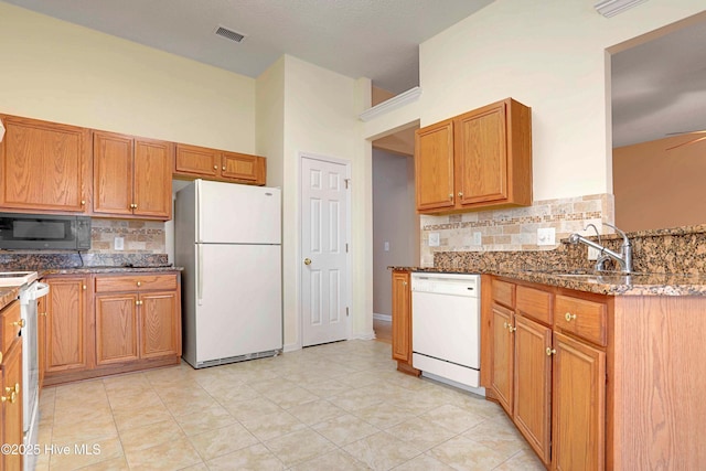 kitchen with dark stone countertops, visible vents, white appliances, light tile patterned flooring, and decorative backsplash