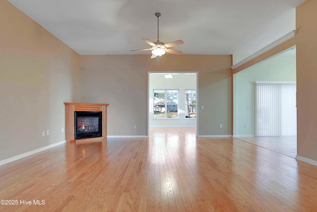 unfurnished living room featuring a glass covered fireplace, light wood-style floors, baseboards, and ceiling fan
