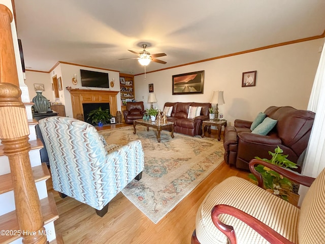 living area featuring a ceiling fan, a fireplace, ornamental molding, and wood finished floors