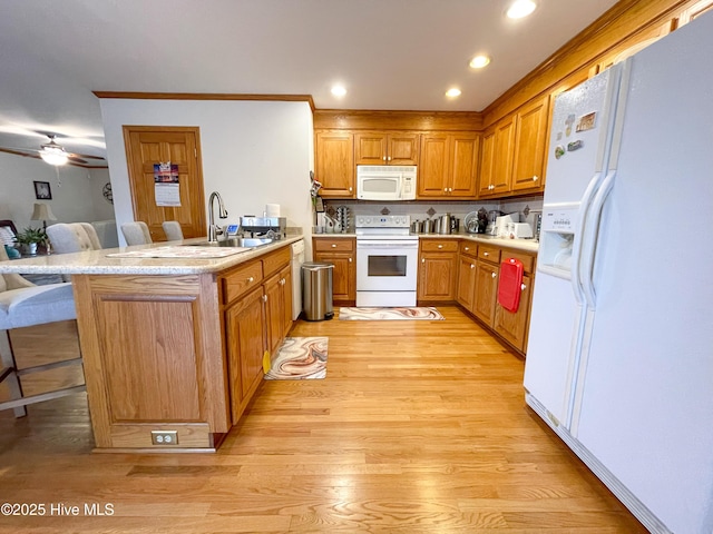 kitchen with light wood-style floors, brown cabinetry, white appliances, a peninsula, and a kitchen breakfast bar