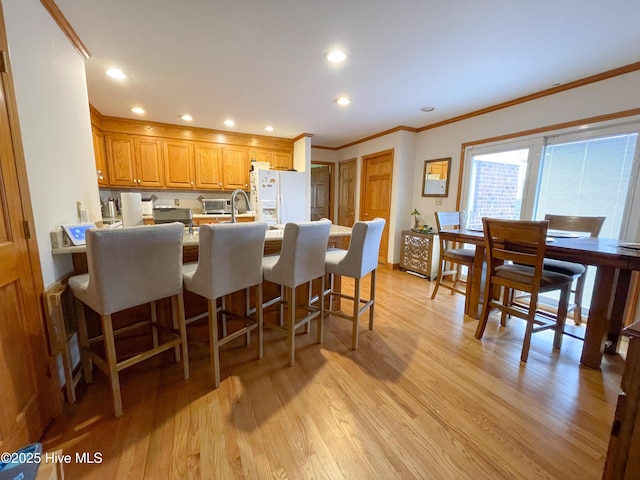 kitchen featuring a breakfast bar area, a peninsula, white refrigerator with ice dispenser, light wood-type flooring, and crown molding