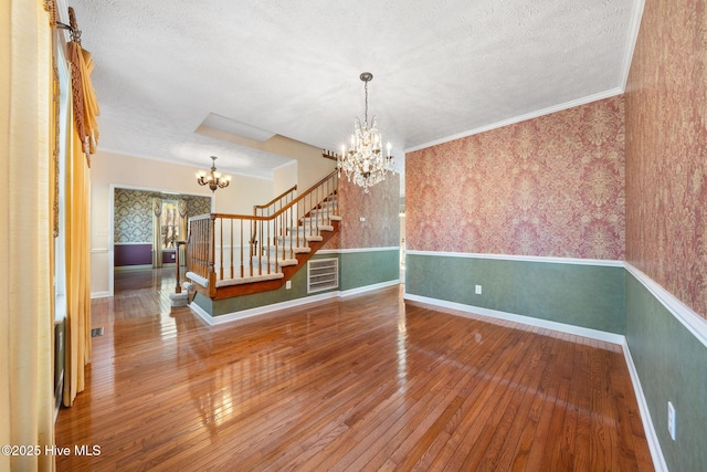 empty room featuring wood-type flooring, stairway, an inviting chandelier, and wallpapered walls