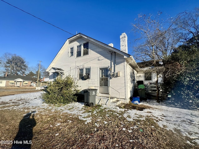 snow covered back of property featuring entry steps and a chimney