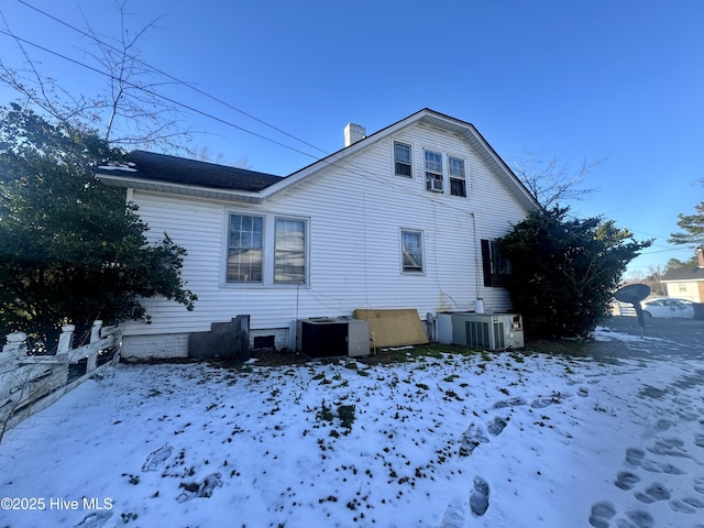 view of snow covered exterior with central air condition unit and a chimney