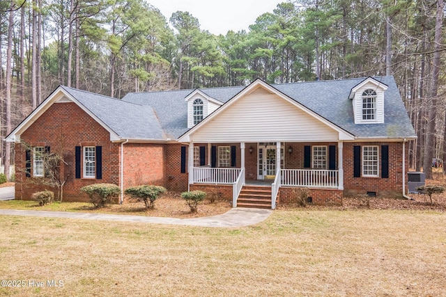 new england style home featuring brick siding, roof with shingles, a porch, a front yard, and crawl space