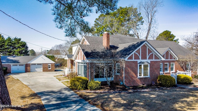 tudor home featuring a garage, a shingled roof, a chimney, an outbuilding, and brick siding