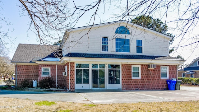 rear view of property featuring a shingled roof, brick siding, and a patio