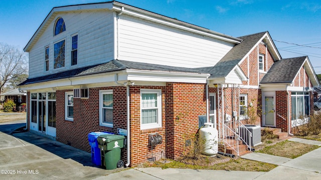 view of property exterior with central air condition unit, driveway, a shingled roof, and brick siding