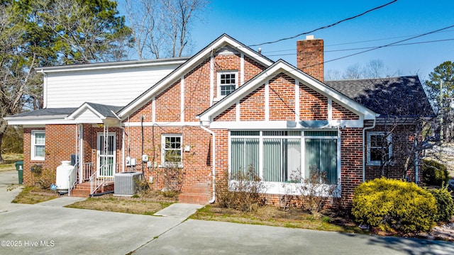 view of front of home with cooling unit, brick siding, and a chimney