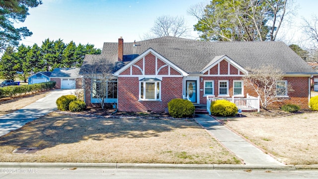 tudor-style house with a shingled roof, concrete driveway, brick siding, and a chimney