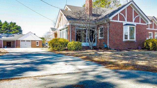 view of front facade featuring a garage, driveway, brick siding, and a chimney