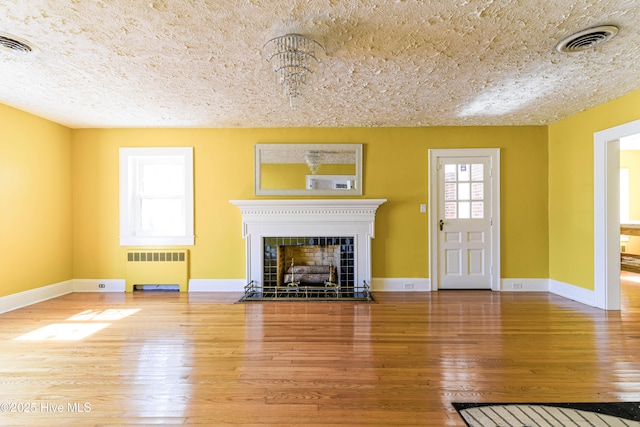 unfurnished living room with a fireplace with flush hearth, visible vents, radiator heating unit, and wood finished floors