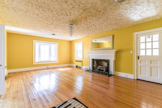 unfurnished living room with radiator, baseboards, wood-type flooring, and a tiled fireplace