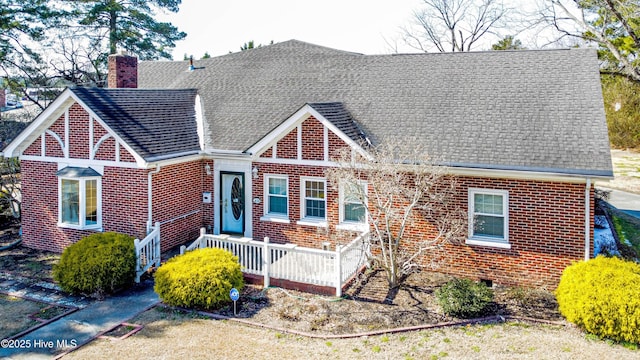 tudor house with roof with shingles, a chimney, and brick siding