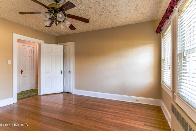 empty room featuring baseboards, a textured ceiling, radiator heating unit, and wood finished floors