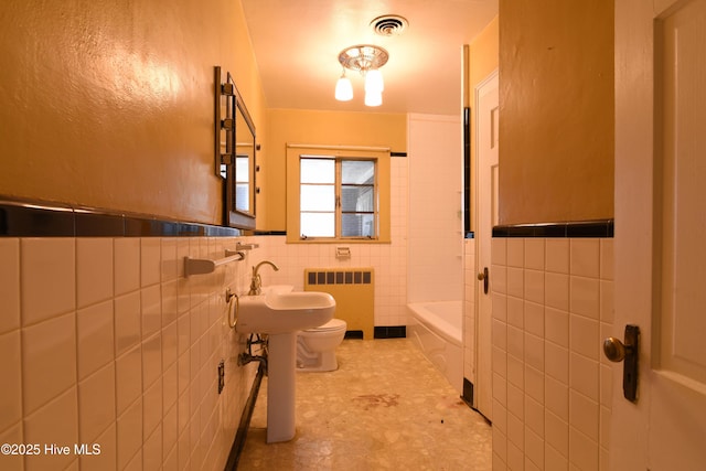 full bath featuring toilet, a washtub, visible vents, tile walls, and radiator heating unit