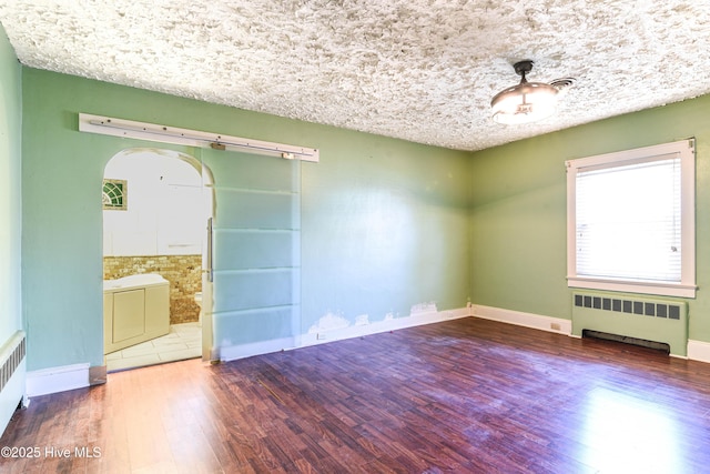 empty room with arched walkways, baseboards, radiator heating unit, and wood finished floors