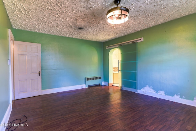 empty room with arched walkways, baseboards, dark wood-style floors, radiator heating unit, and a textured ceiling