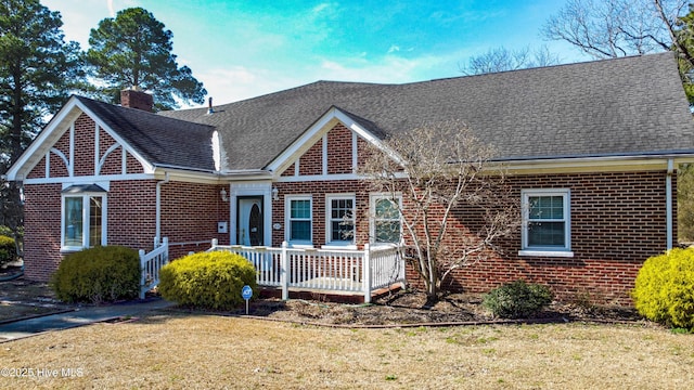 view of front facade featuring brick siding, a chimney, a front lawn, and roof with shingles