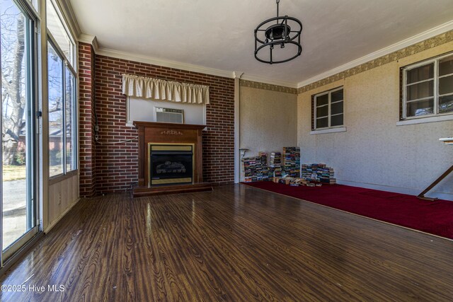 unfurnished living room featuring a fireplace with raised hearth, ornamental molding, plenty of natural light, and wood finished floors