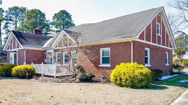 exterior space with brick siding, a yard, a chimney, a shingled roof, and a deck