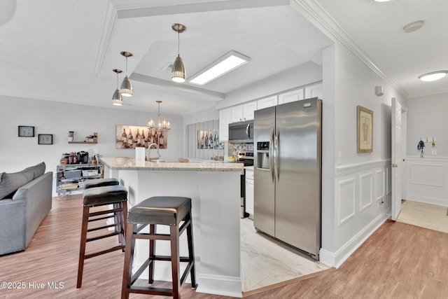 kitchen with open floor plan, stainless steel appliances, crown molding, white cabinetry, and a decorative wall