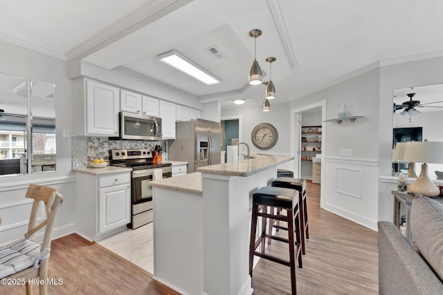 kitchen featuring stainless steel appliances, visible vents, crown molding, light wood-style flooring, and ceiling fan